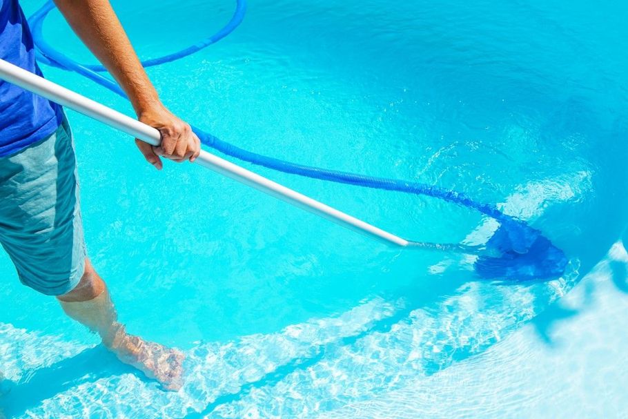 Person cleaning a bright blue pool with a long-handled net