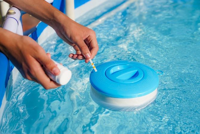 Hands testing a blue inflatable pool float in a swimming pool with a small bottle nearby