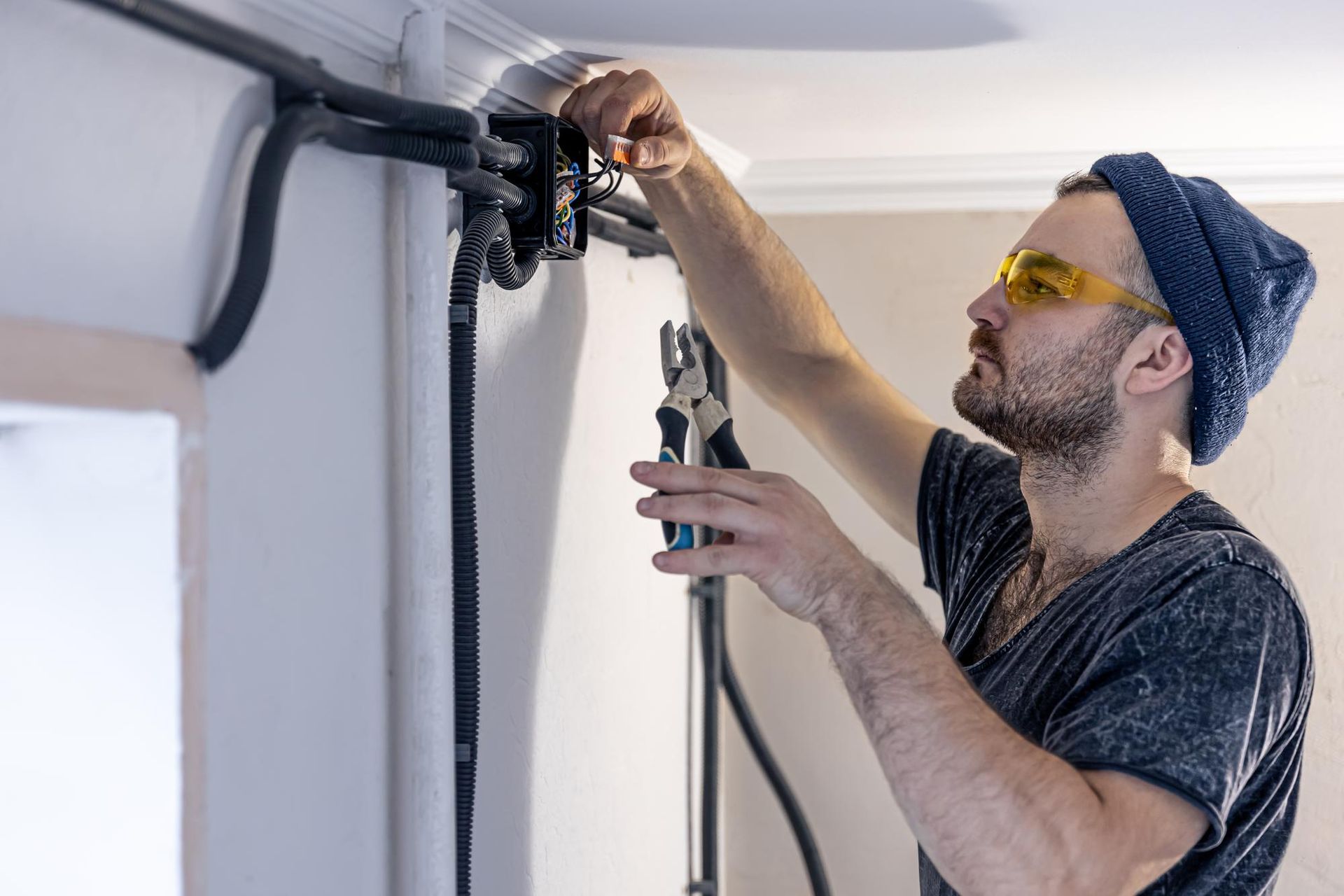Man installing a ceiling-mounted curtain track with a drill in a white room