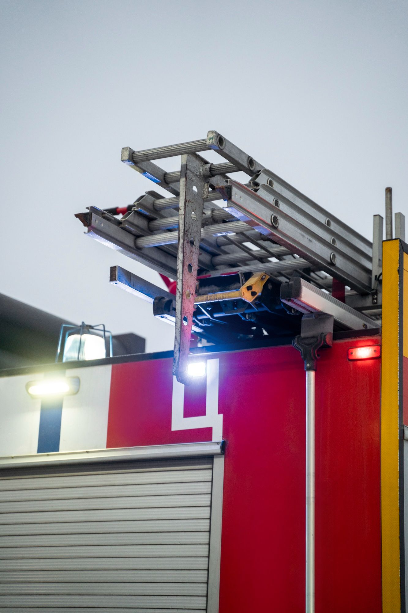 Worker on a roof using a ladder platform beside a red building at dusk