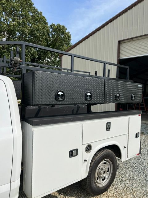 White pickup truck with black utility toolboxes parked beside a building and gravel driveway