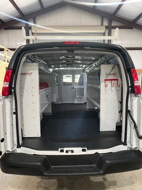 Interior of a cargo van with white storage cabinets, metal racks, and a black floor mat in a garage.