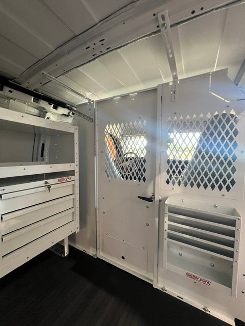 Inside a white utility van, showing storage drawers and a mesh partition with vents.