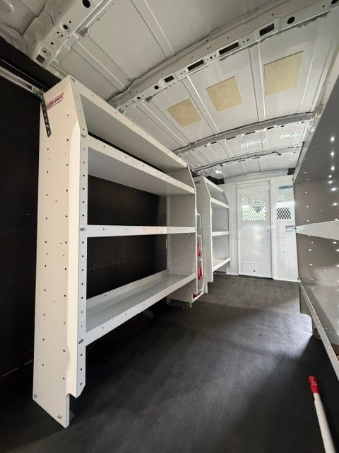 Empty cargo van interior with white shelving, black floor, and open rear doors
