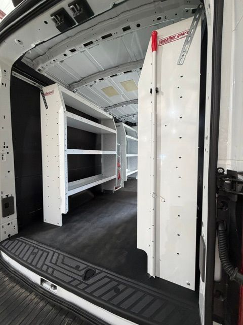 White cargo van interior with built-in shelving and black floor mat, viewed from the open rear doors