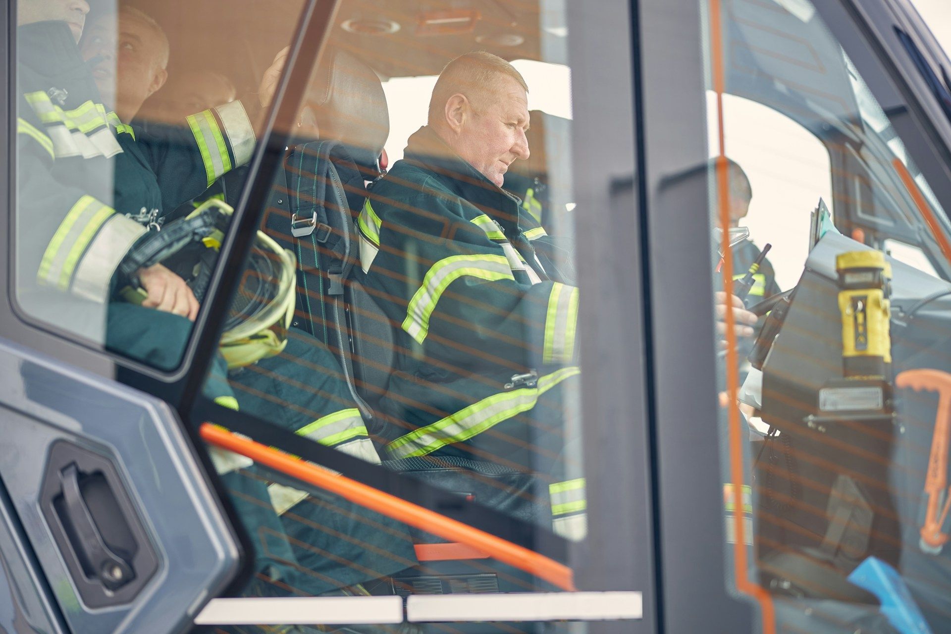Firefighters in high-visibility gear seated inside a vehicle cab