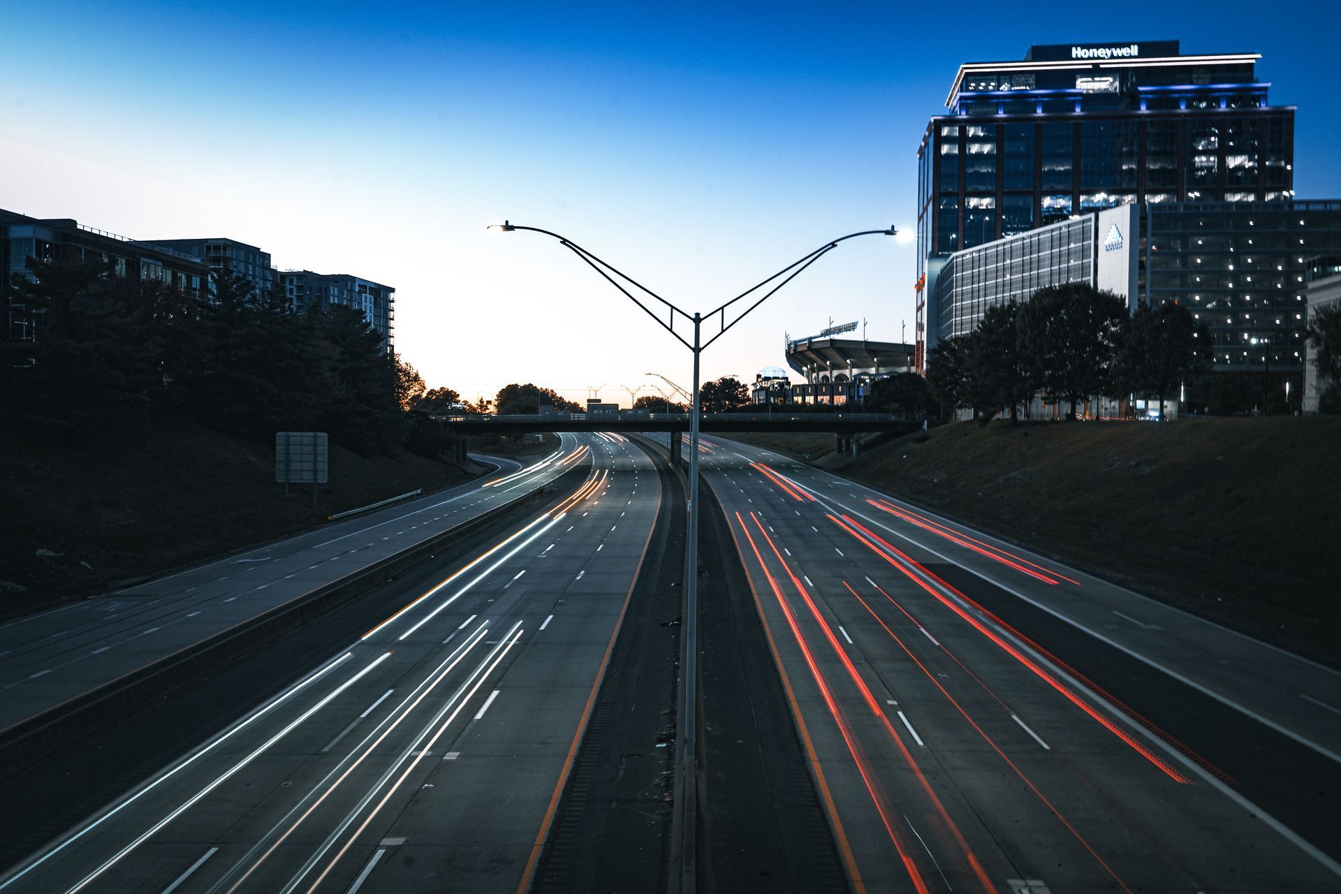 Highway at dusk with light trails and city buildings silhouetted against a blue sky