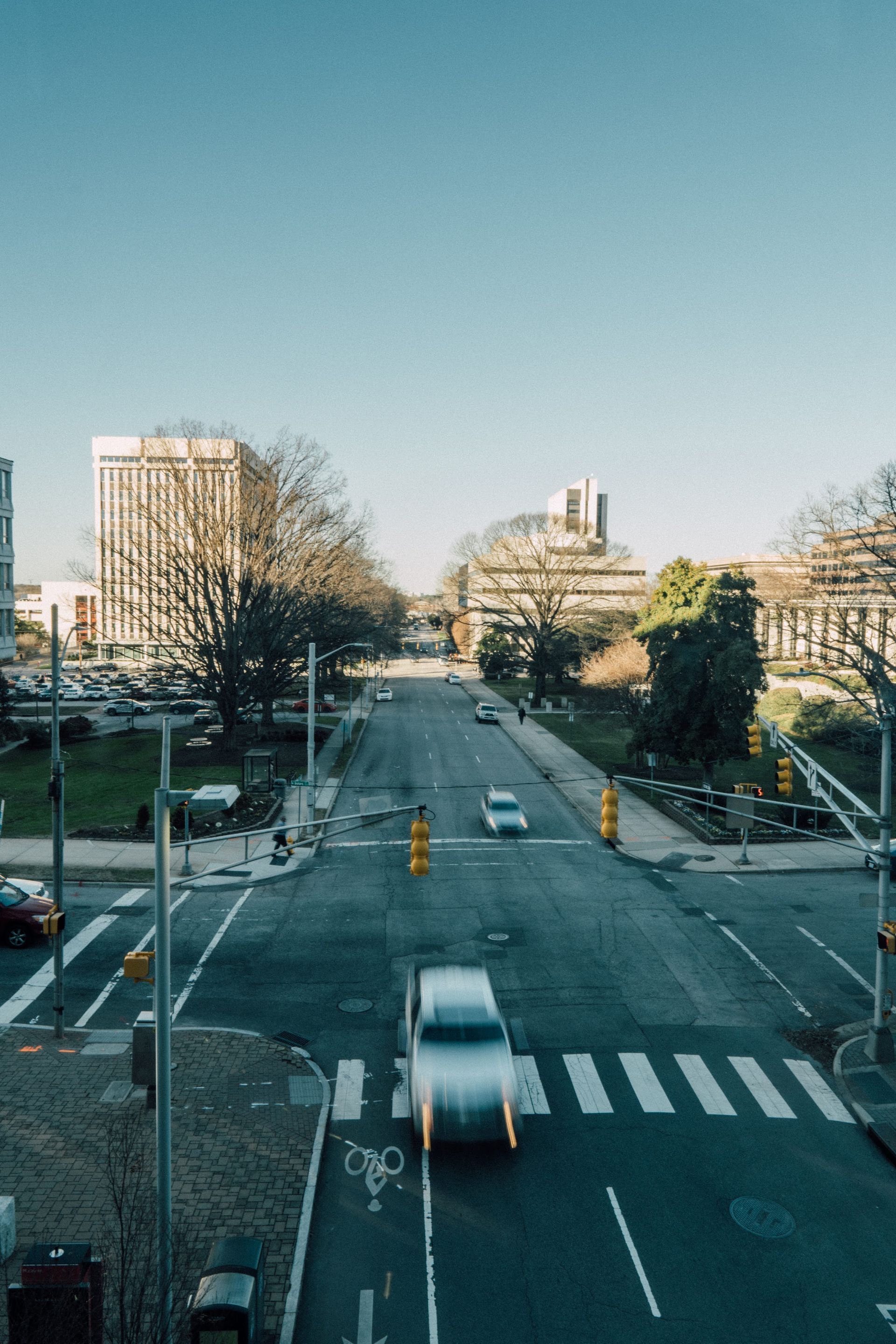 Wide city street with light traffic and buildings under a clear blue sky