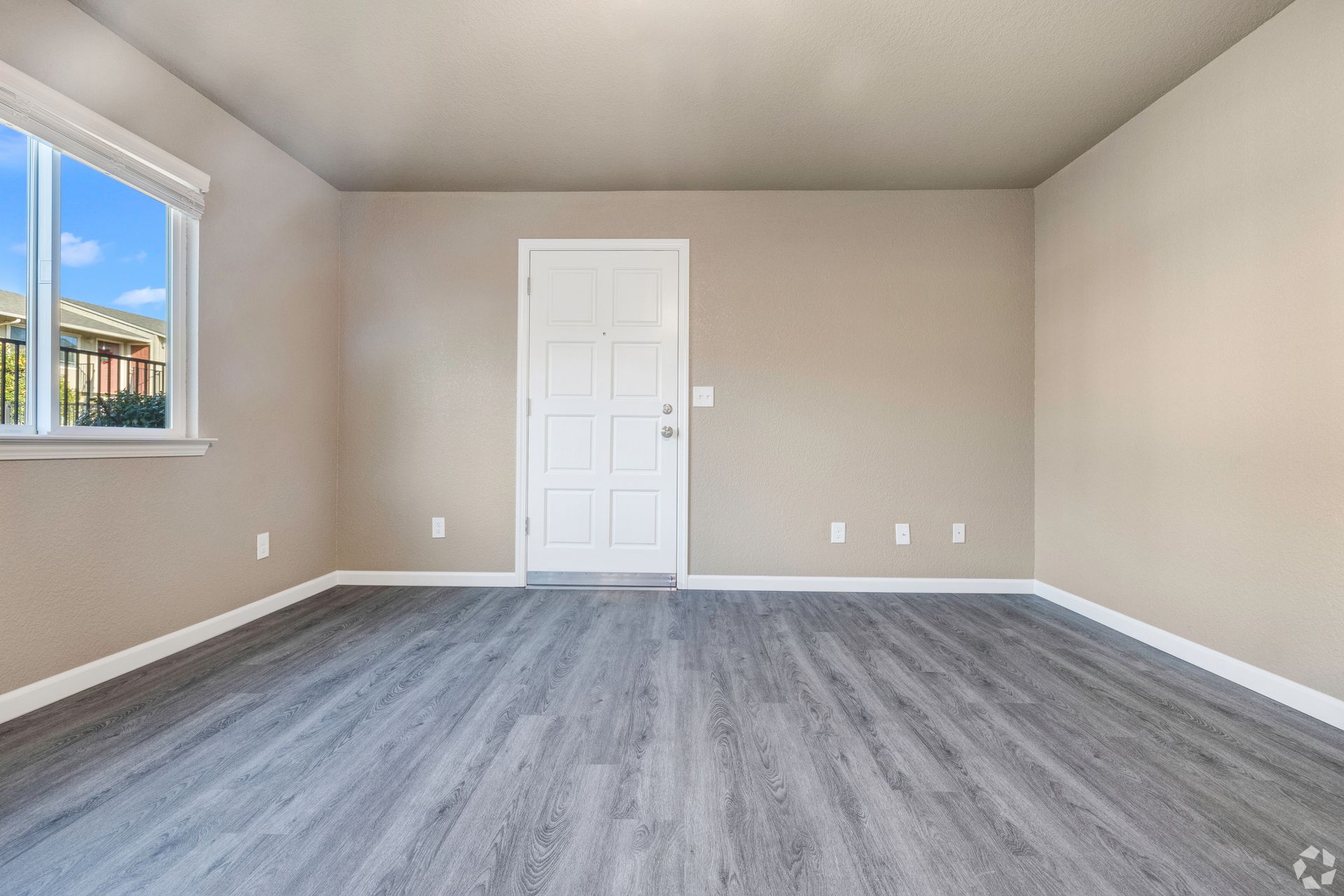 Empty room with gray floor, beige walls, white door, and window.