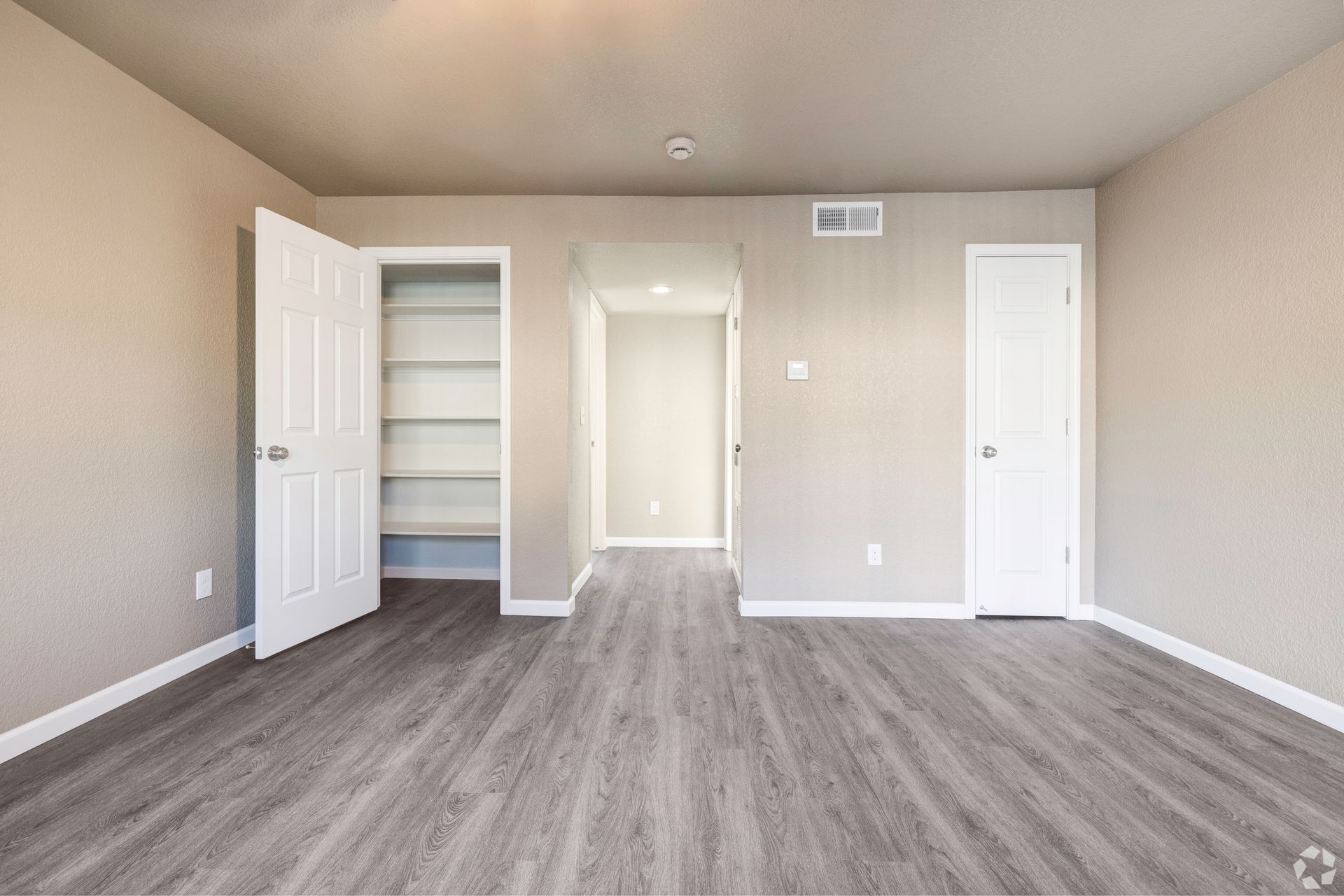 Empty room with gray flooring, beige walls, and white doors leading to a closet and hallway.