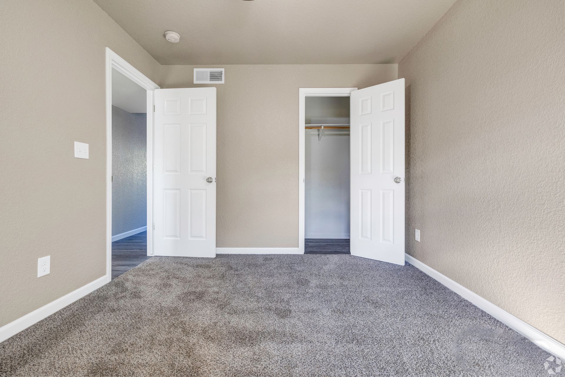 Empty bedroom with gray carpet, beige walls, white doors, and a closet.