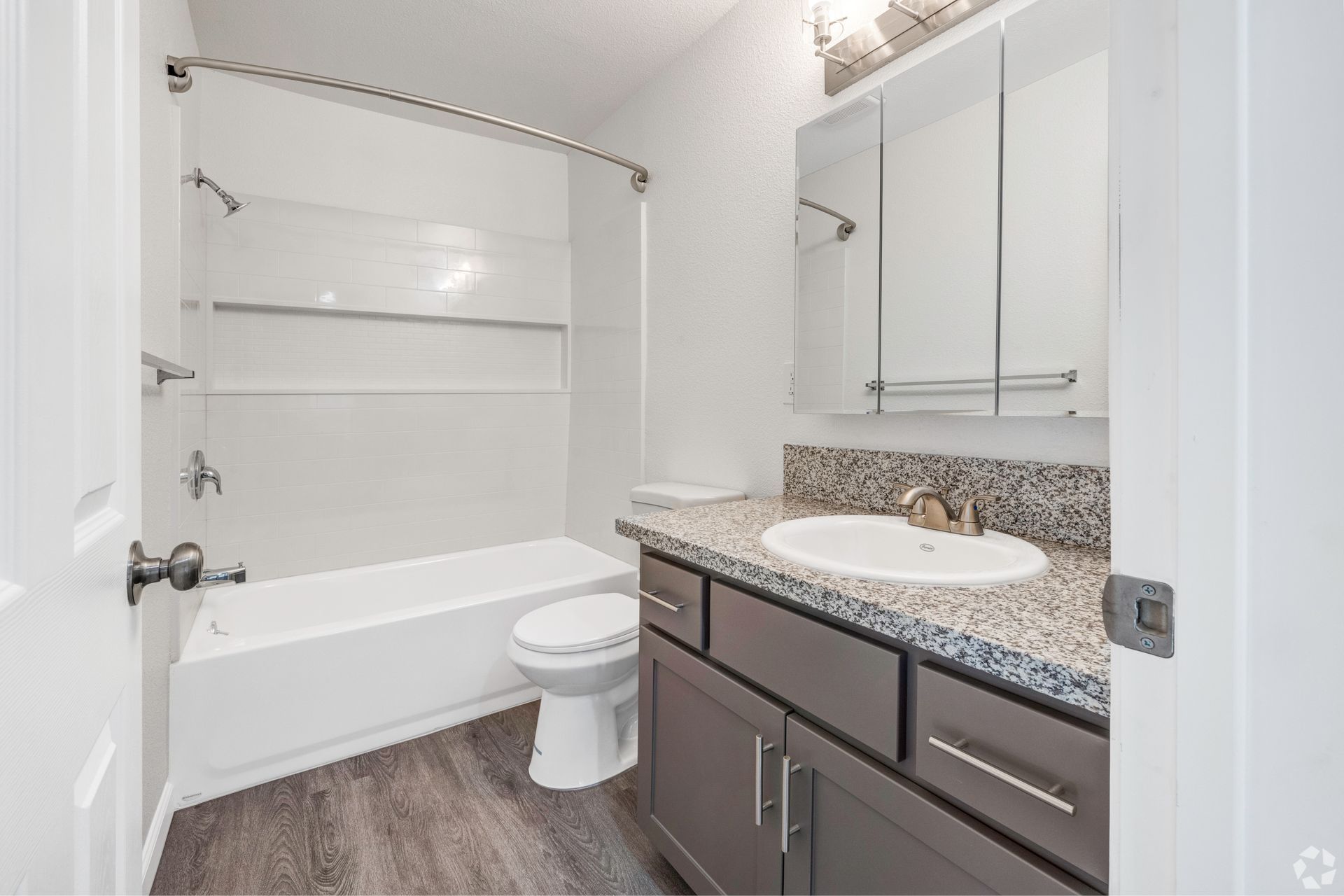 Bathroom with white tub, gray vanity, wood-look floor, and a toilet.