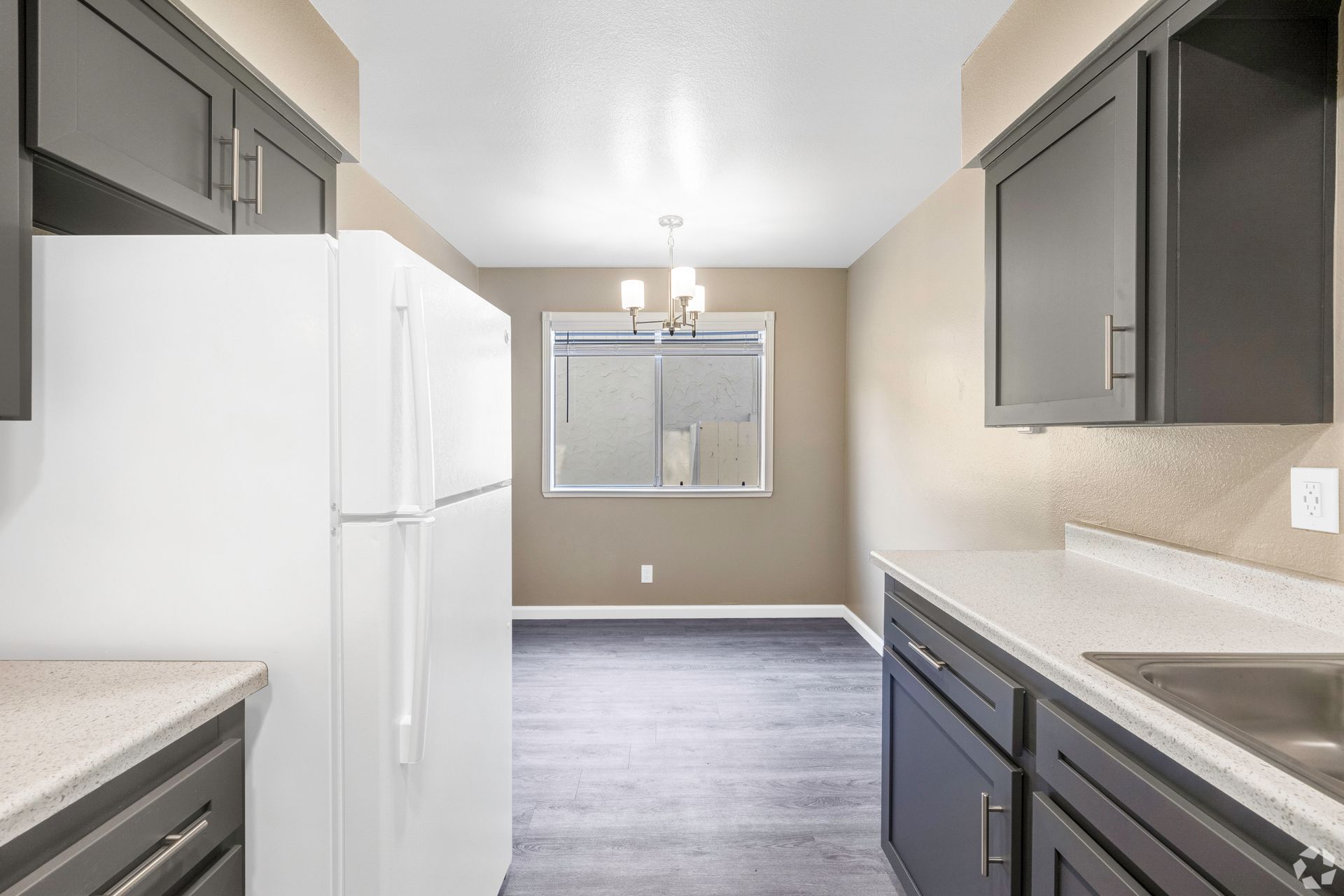 Kitchen with white fridge, dark gray cabinets, and dining area in the background.