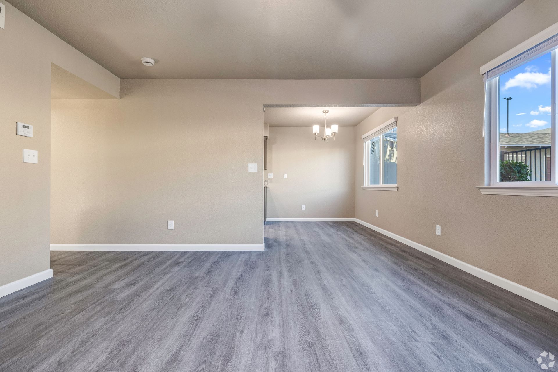 Empty living room with gray wood-look floors, beige walls, and a window with a view of the outdoors.