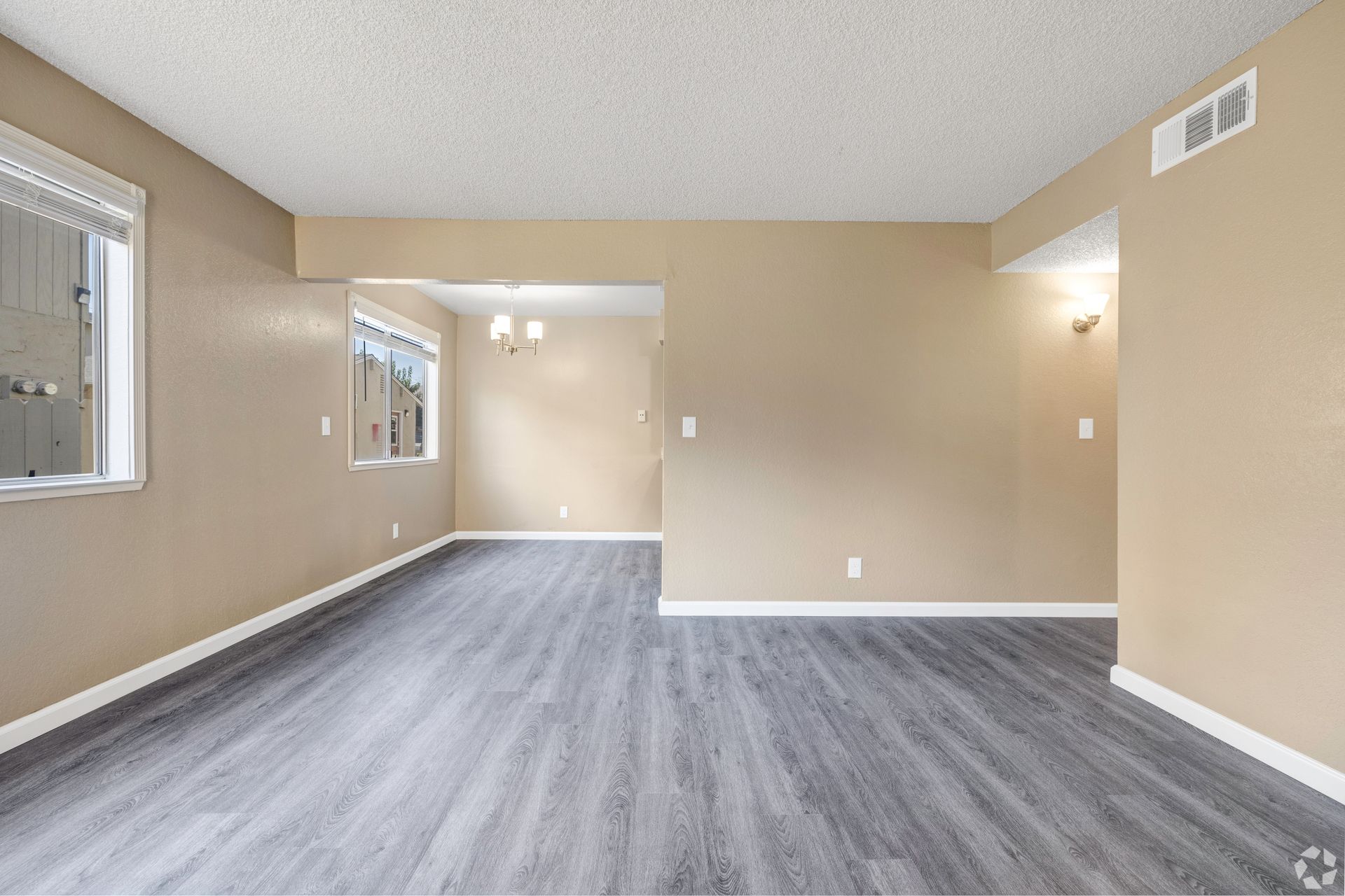 Empty living room with gray wood-look floors and tan walls. White ceiling and trim.