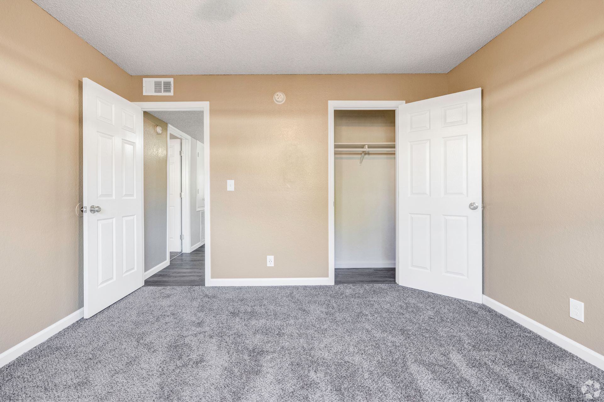 Empty bedroom with neutral walls, gray carpet, white doors and closet, and a hallway entrance.