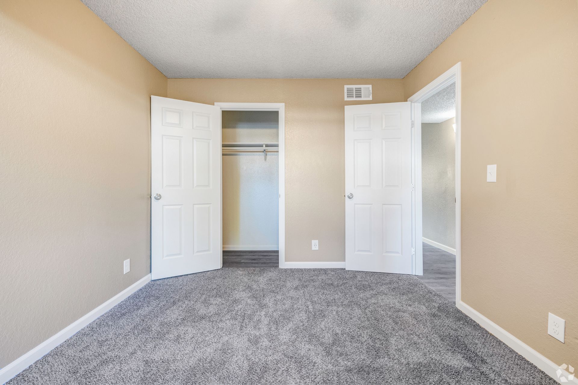 Empty bedroom with beige walls, gray carpet, white doors, and a closet.