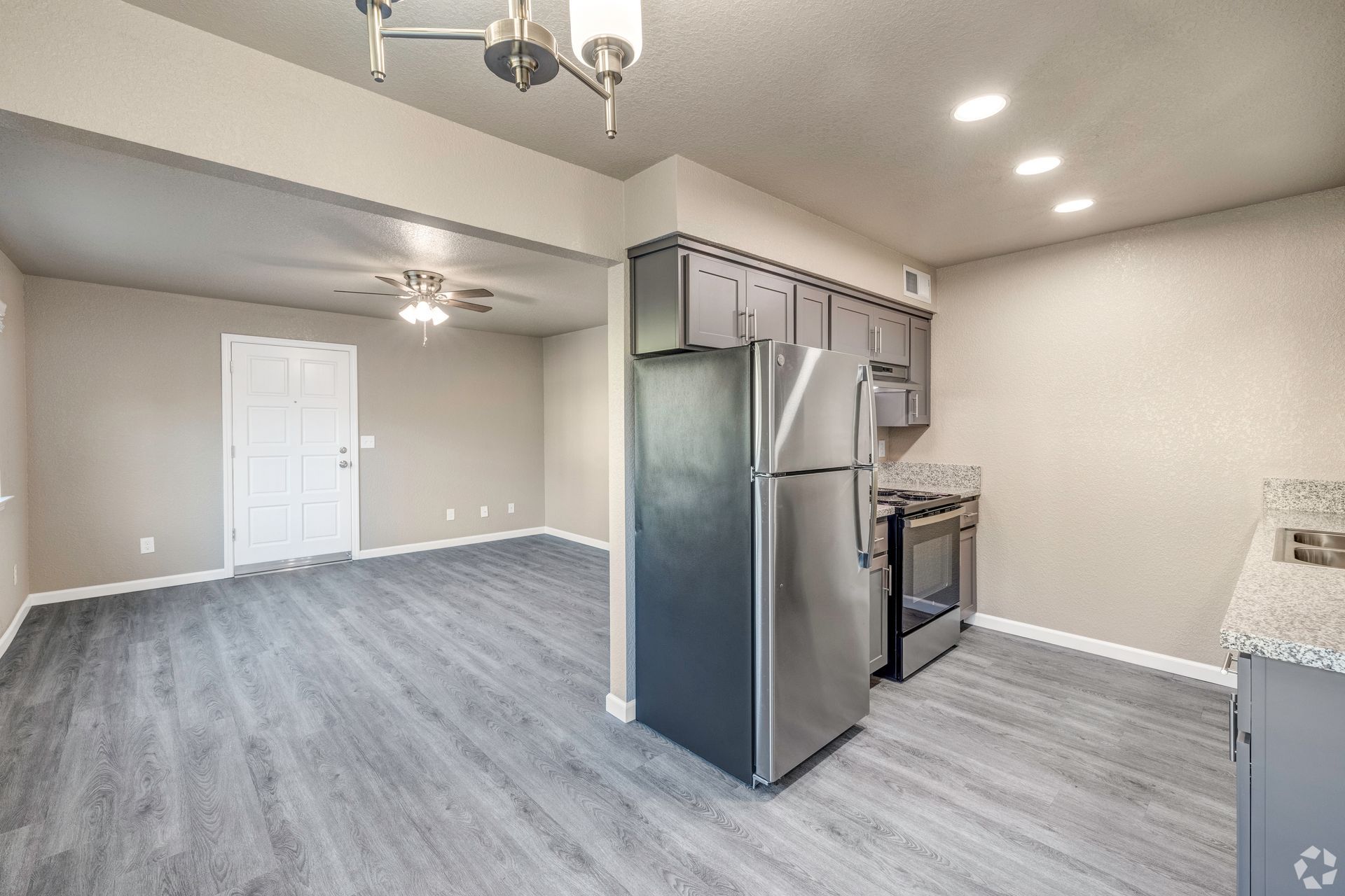 Kitchen and living area with gray cabinets, stainless steel appliances, and gray flooring.