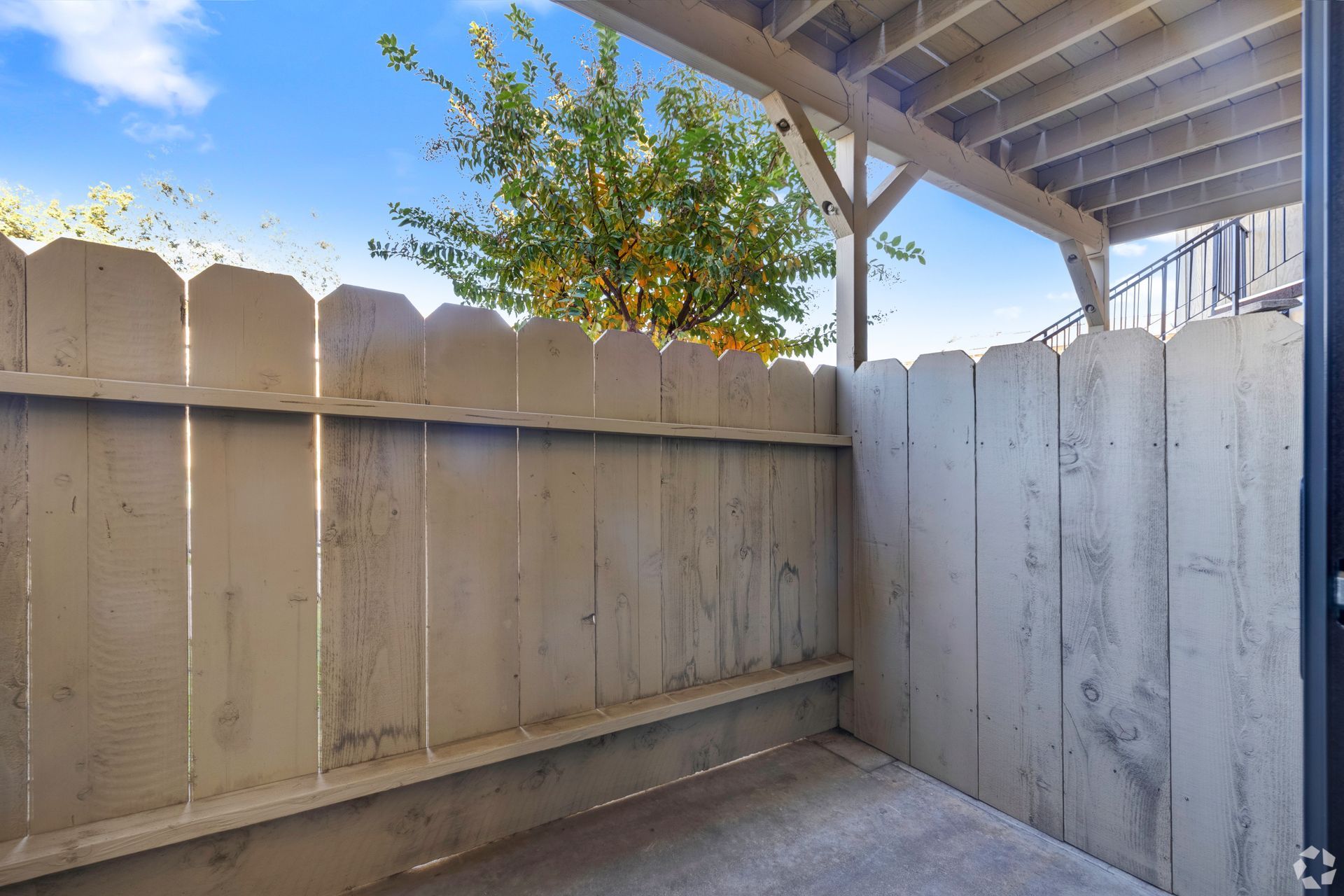 Small, enclosed patio with a white picket fence, concrete floor, and blue sky view.