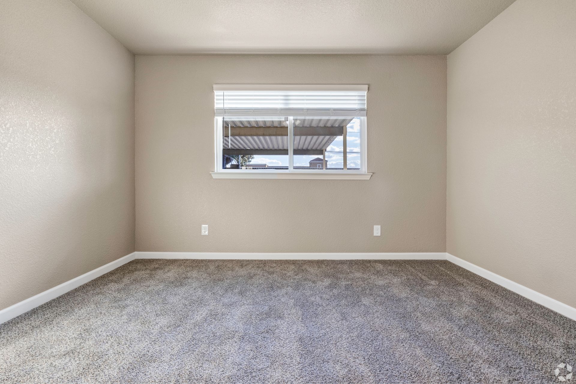Empty room with tan walls, a window, and gray carpet.