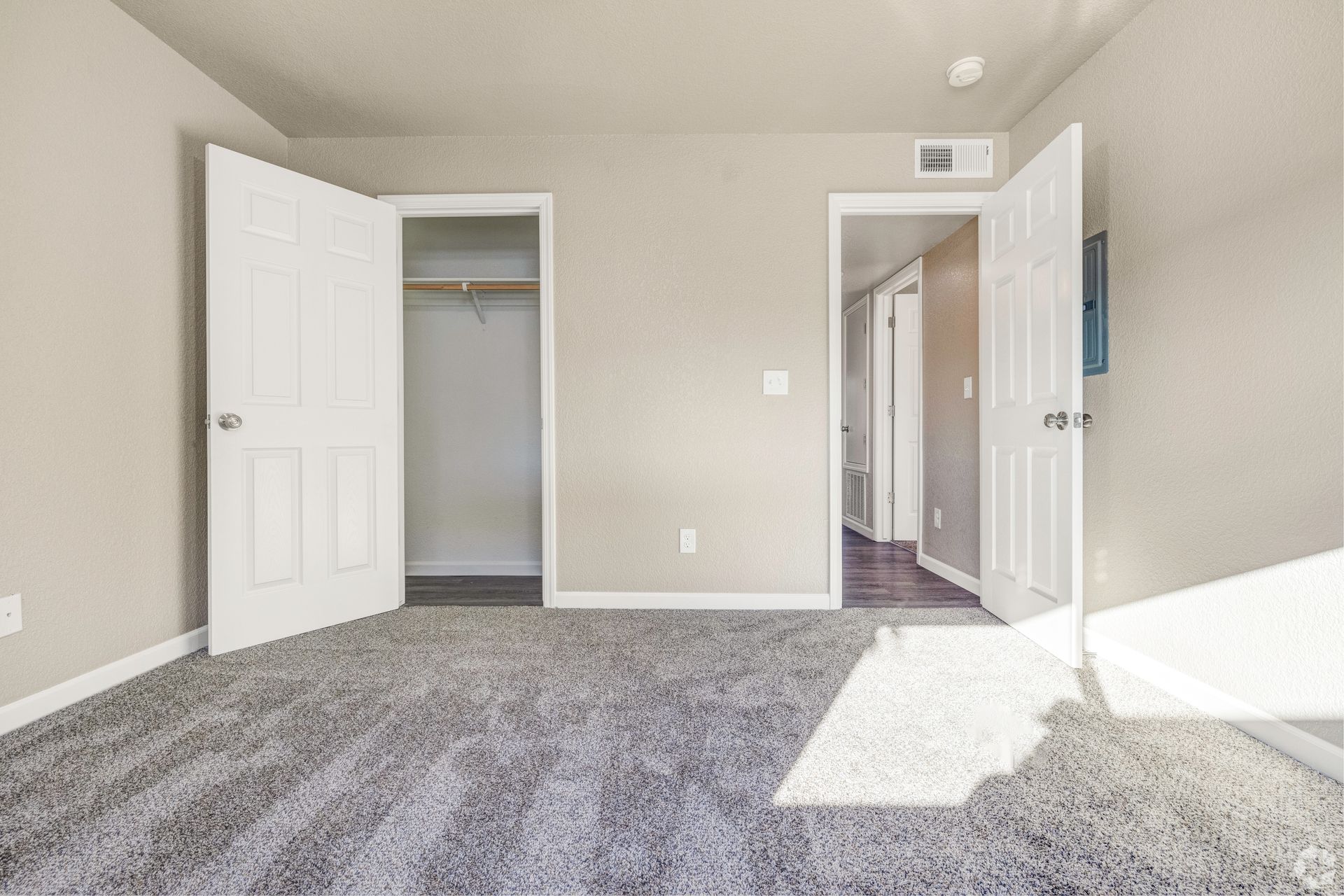 Empty bedroom with gray carpet, white doors, and a closet.