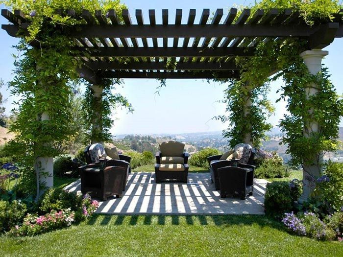CERCOS CRUBER - Pérgola con enredaderas, tres sillones oscuros y vista panorámica, proyectando líneas de sombra en el patio.