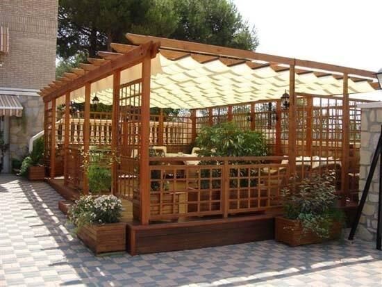 Pérgola de madera con techo ligero de lona, plantas y diseño de celosía cuadrada. Ideal para patio exterior.