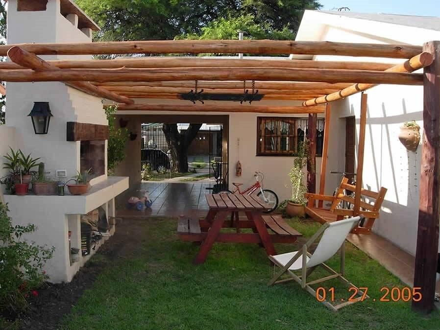 Patio al aire libre con pérgola de madera, parrilla incorporada, mesa de picnic, columpio y sillón.