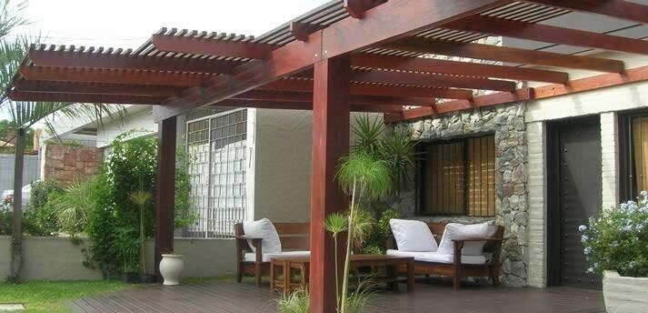 CERCOS CRUBER - Pérgola de madera sobre zona de estar al aire libre con cojines blancos, vegetación y pared de piedra.