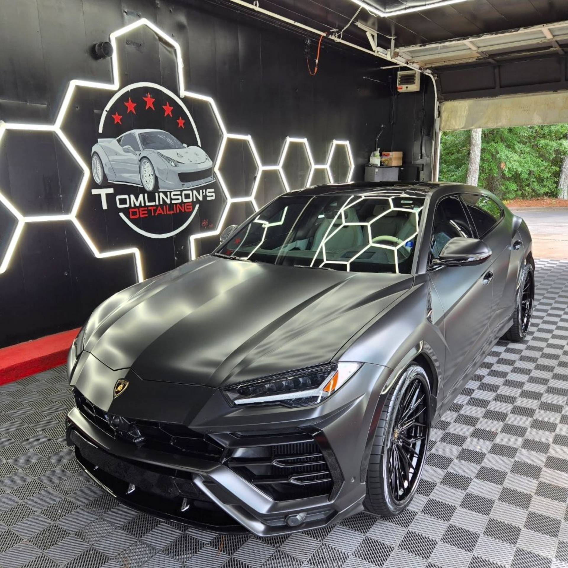 Matte black Lamborghini Urus in a neon-lit showroom with hexagon wall lights and checkered flooring