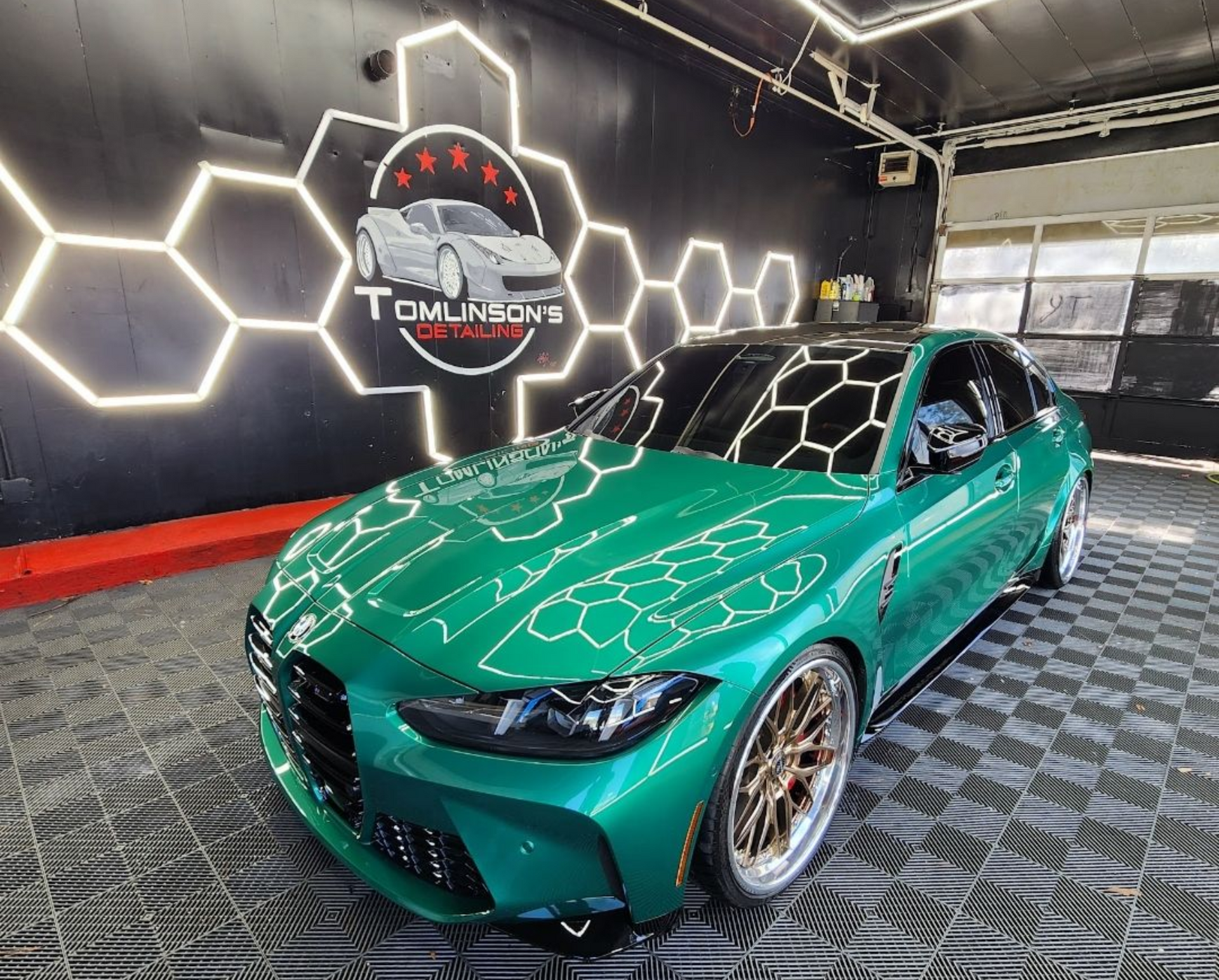 Green sports coupe in a detailing garage with hexagon wall lights and a diamond-pattern floor