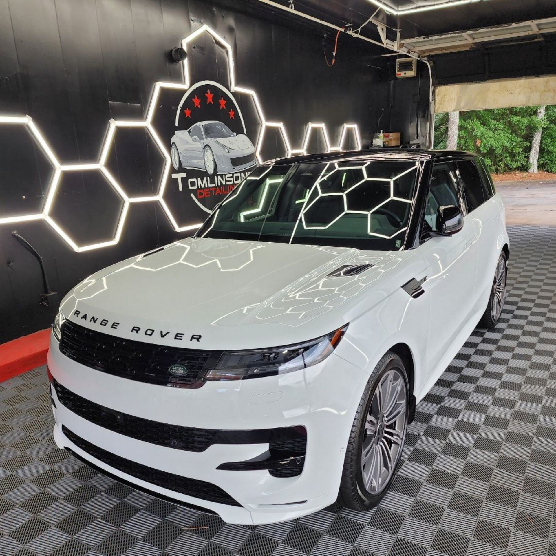 White Range Rover SUV in a showroom with hexagonal wall lights and patterned floor.