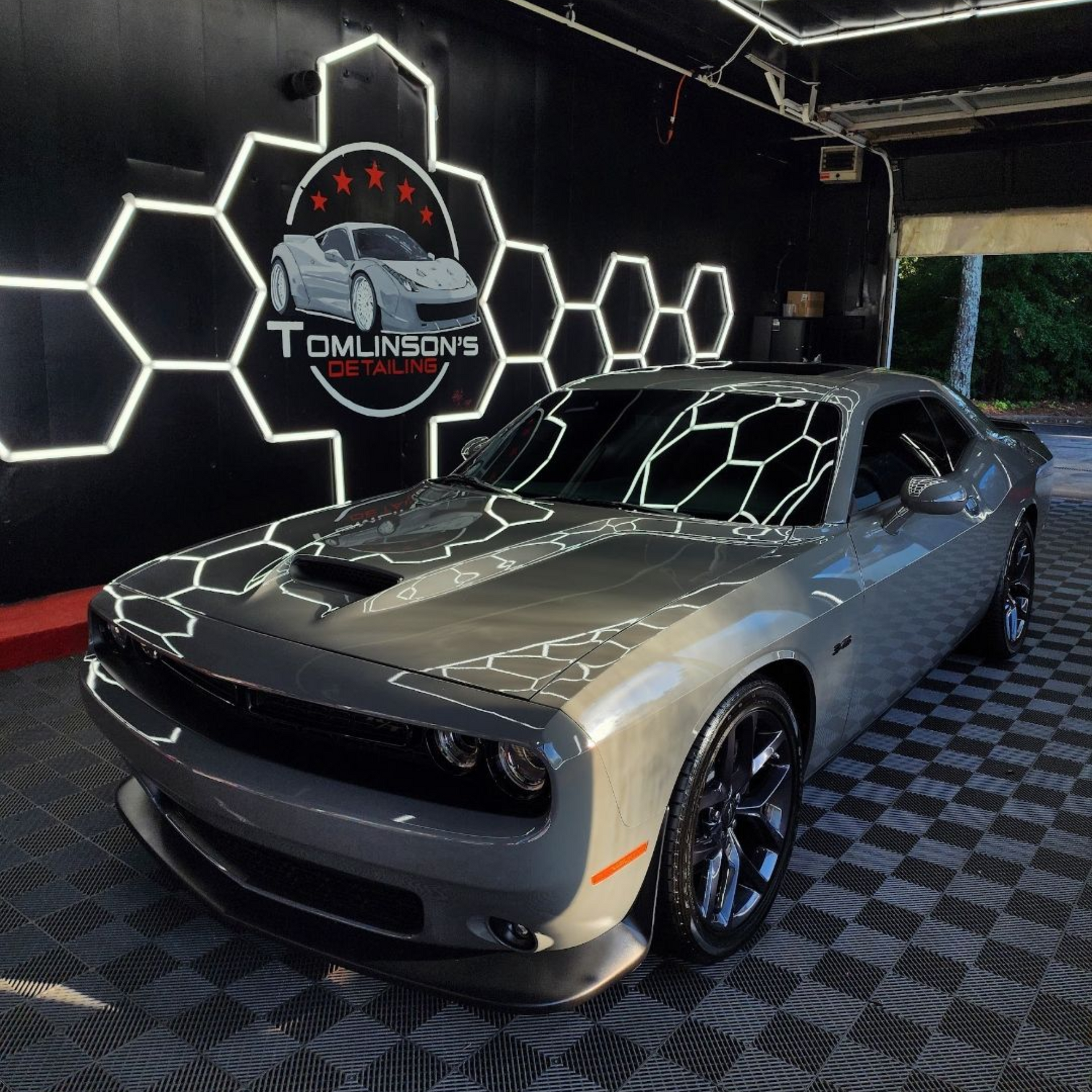 Silver classic muscle car in a neon-lit showroom with hexagonal wall lights and a Tomlinson’s sign