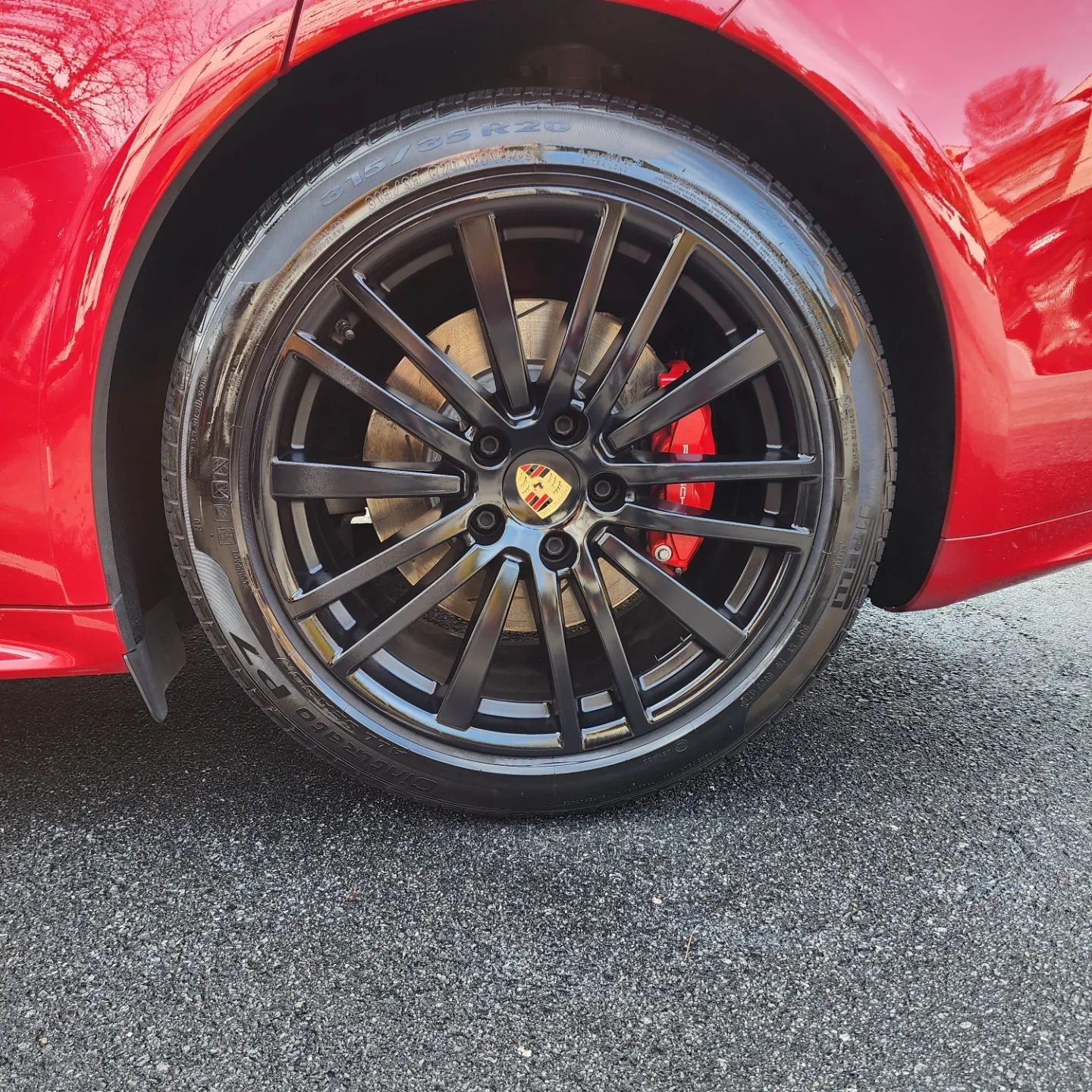 Red car wheel with black rim and red brake caliper. Porsche logo on hubcap.