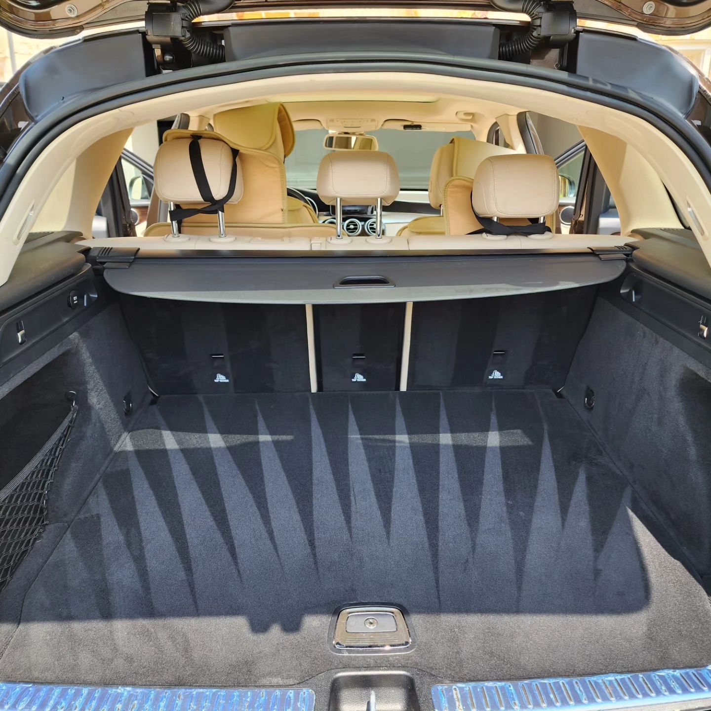 Open trunk of a beige Mercedes SUV with black carpet and tan leather seats visible.
