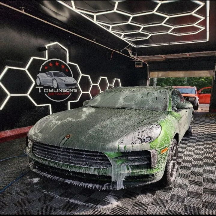 Green car covered in soap at a car wash with Tomlinson's logo on wall.