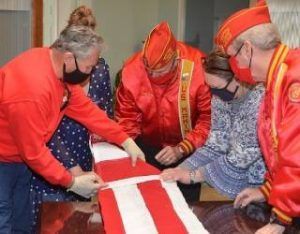 People in red jackets and masks folding a red-and-white cloth around a table