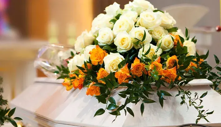 White and yellow funeral flowers arranged on a off white casket