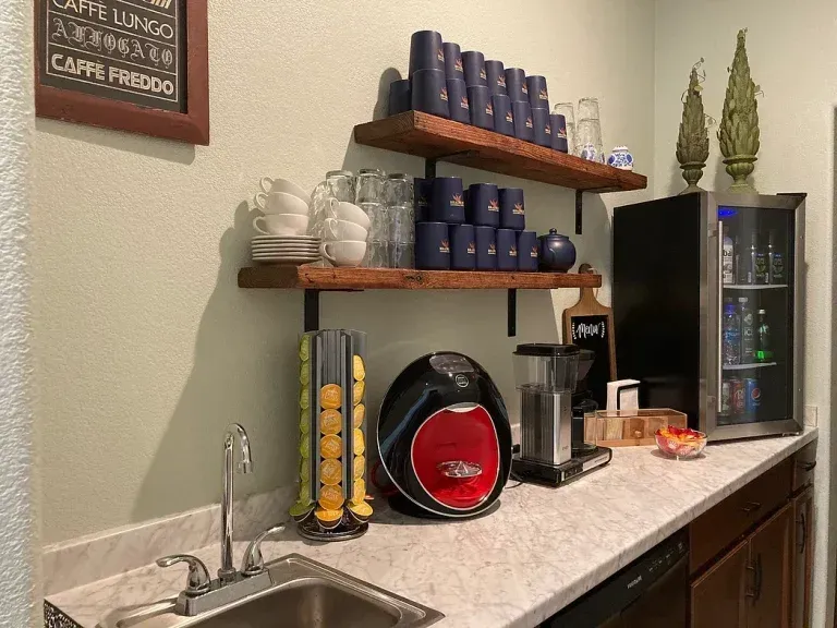 Coffee station with mugs, pods, espresso machine, and mini fridge on a countertop.