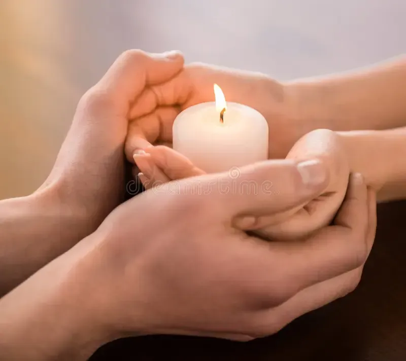 soft big hands holding smaller soft hands in which lit candle is being held on top of table
