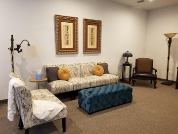 Living room with patterned sofa, teal ottoman, chair, floor lamps, and framed wall art