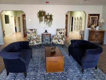 Elegant living room with navy velvet chairs, patterned rugs, and decorative wall wreaths.