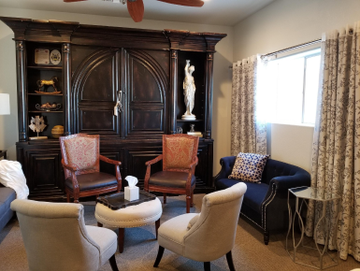 Elegant living room with dark wood armoire, white chairs, red armchairs, and a bright window with curtains