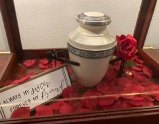 Memorial display with white urn, red roses, and framed note reading “always my father forever in my heart.”