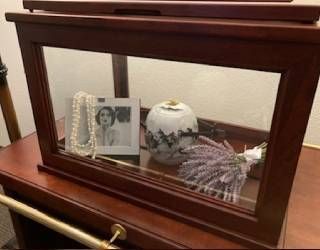 Framed memorial display with photo, rosary, urn, and lavender flowers in a wooden case