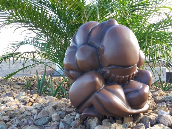 Abstract bronze sculpture on rocks in a garden with palm fronds behind it