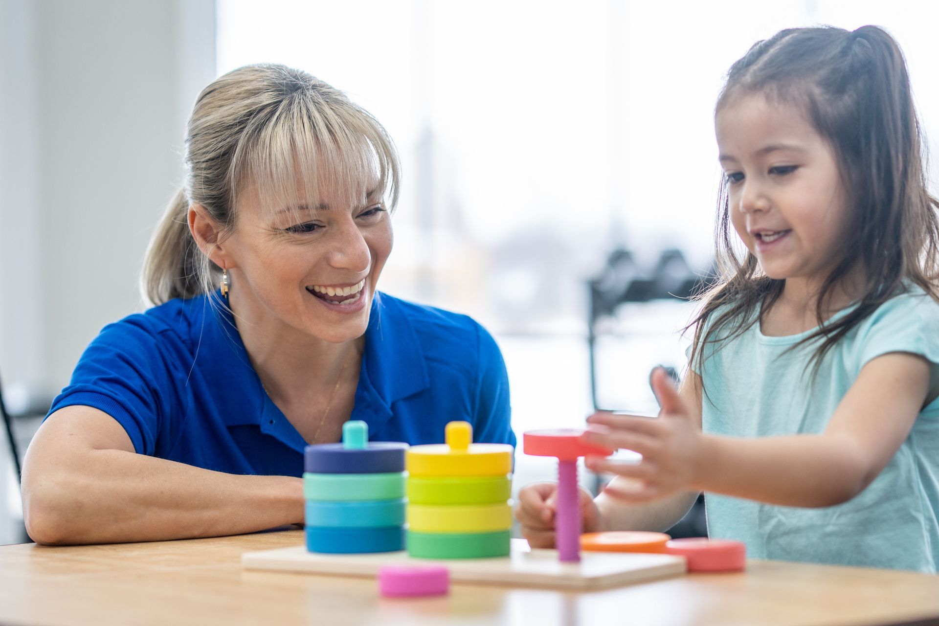 A woman and a little girl are playing with toys at a table.