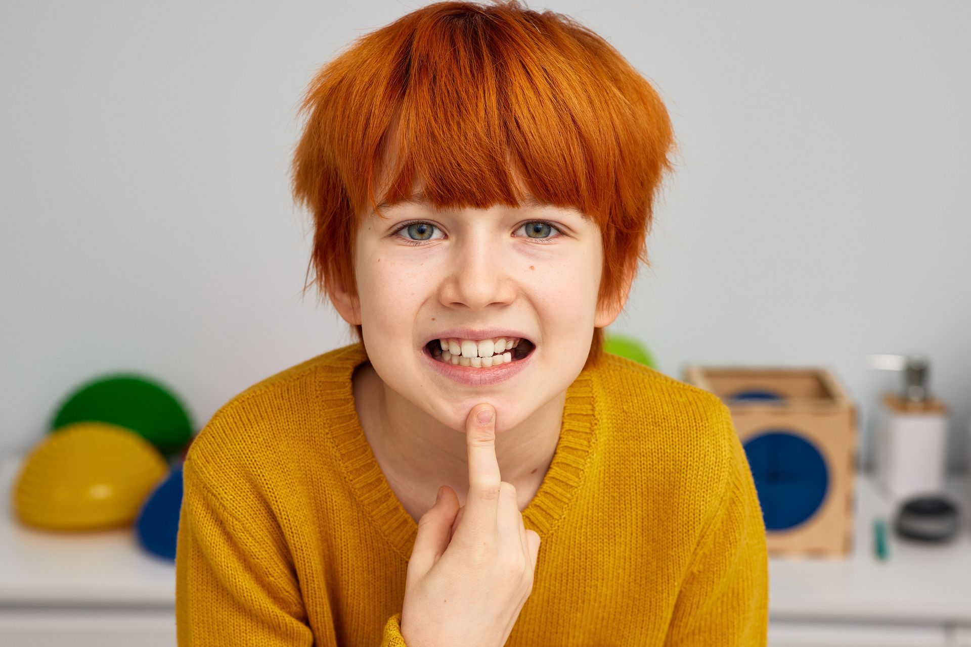 A young boy with red hair is smiling and pointing at his teeth. A young boy with red hair is smiling and pointing at his teeth.