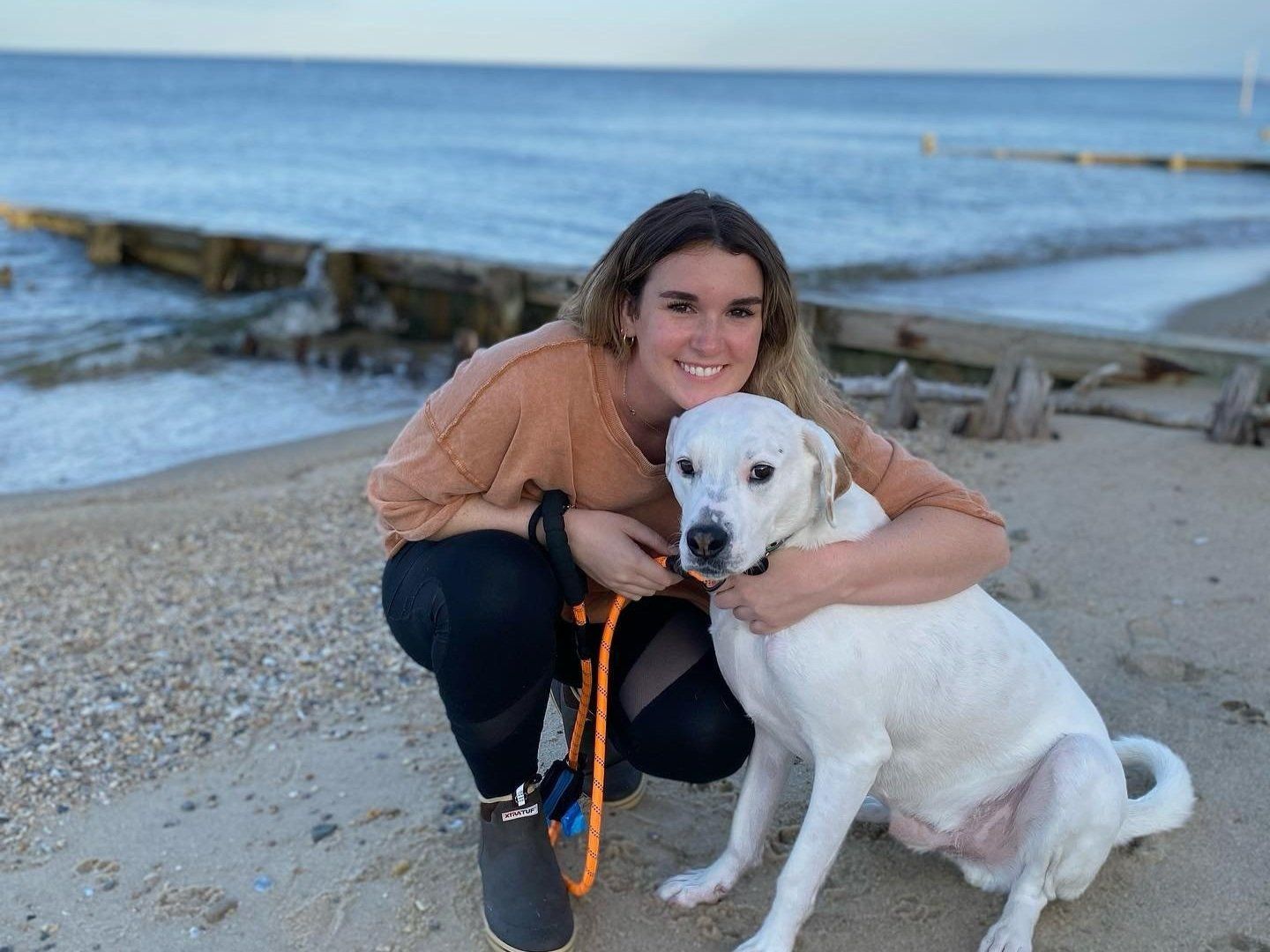A woman is hugging a white dog on the beach. A woman is hugging a white dog on the beach.
