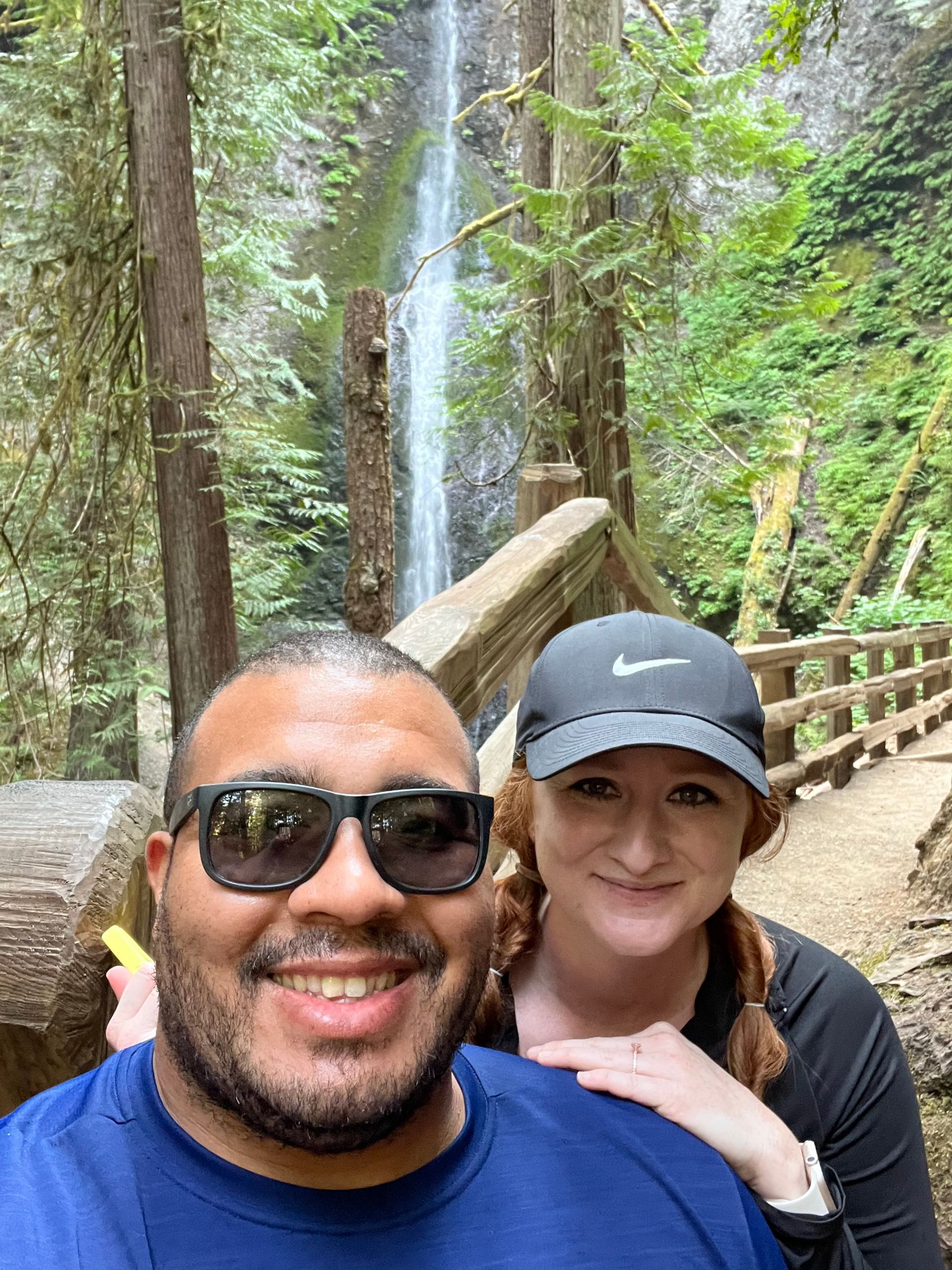 A man and a woman are posing for a picture in front of a waterfall. A man and a woman are posing for a picture in front of a waterfall.